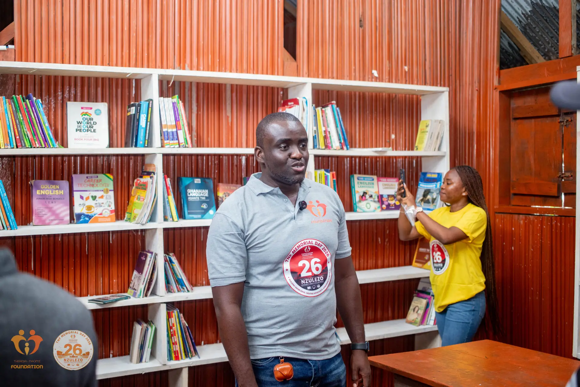Project Nzulezo: From Vision to Reality TNF representative speaking beside bookshelves in the Nzulezo Community Library during commissioning.